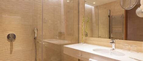 Un baño moderno con ducha envuelta en cristal, un lavabo blanco y un espejo grande.