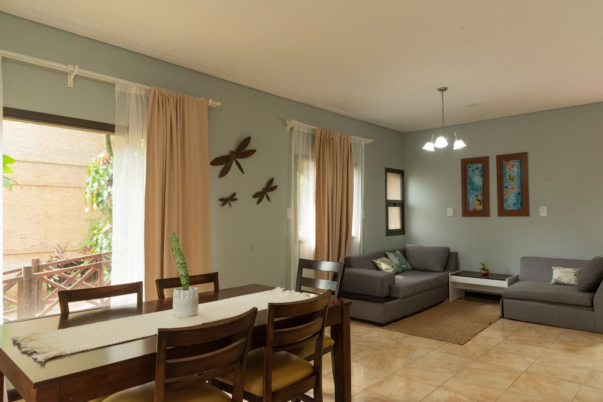 A living room with a dining area, a gray sofa, a coffee table, and a potted plant.