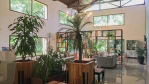 A spacious indoor area with wooden furniture, large windows, and various plants. - Village Cataratas (Puerto Iguazú)