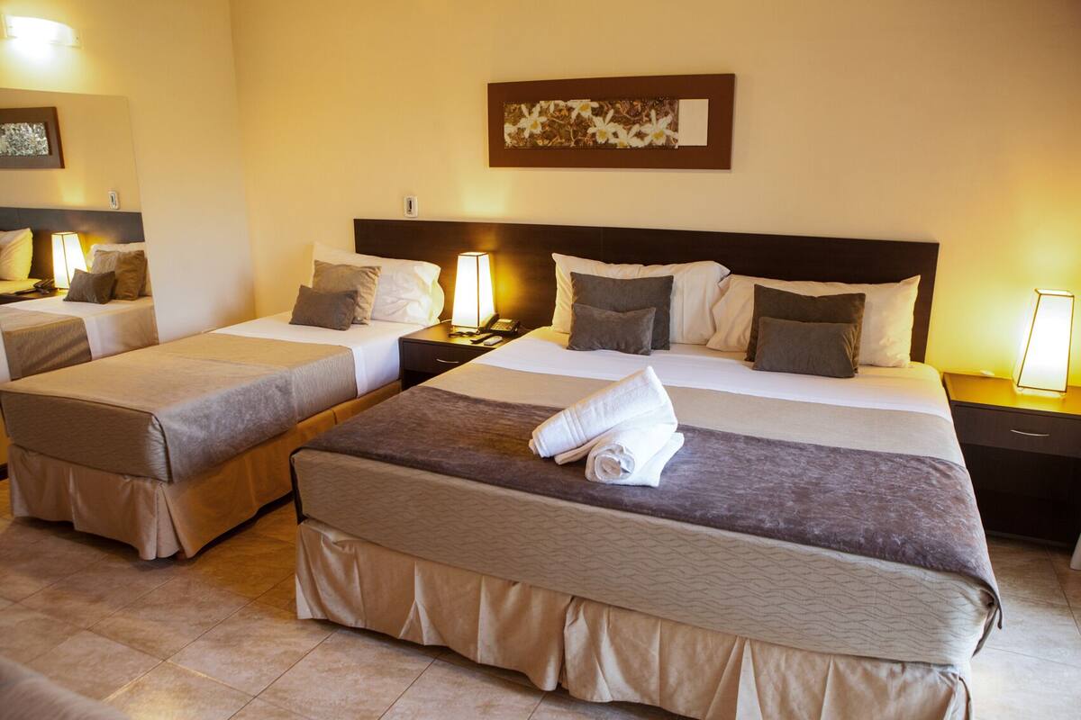 A hotel room with two beds, each with a headboard, bedside lamps, and a folded towel on the beds.