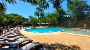 A pool area with lounge chairs and umbrellas, surrounded by trees. - Village Cataratas (Puerto Iguazú)
