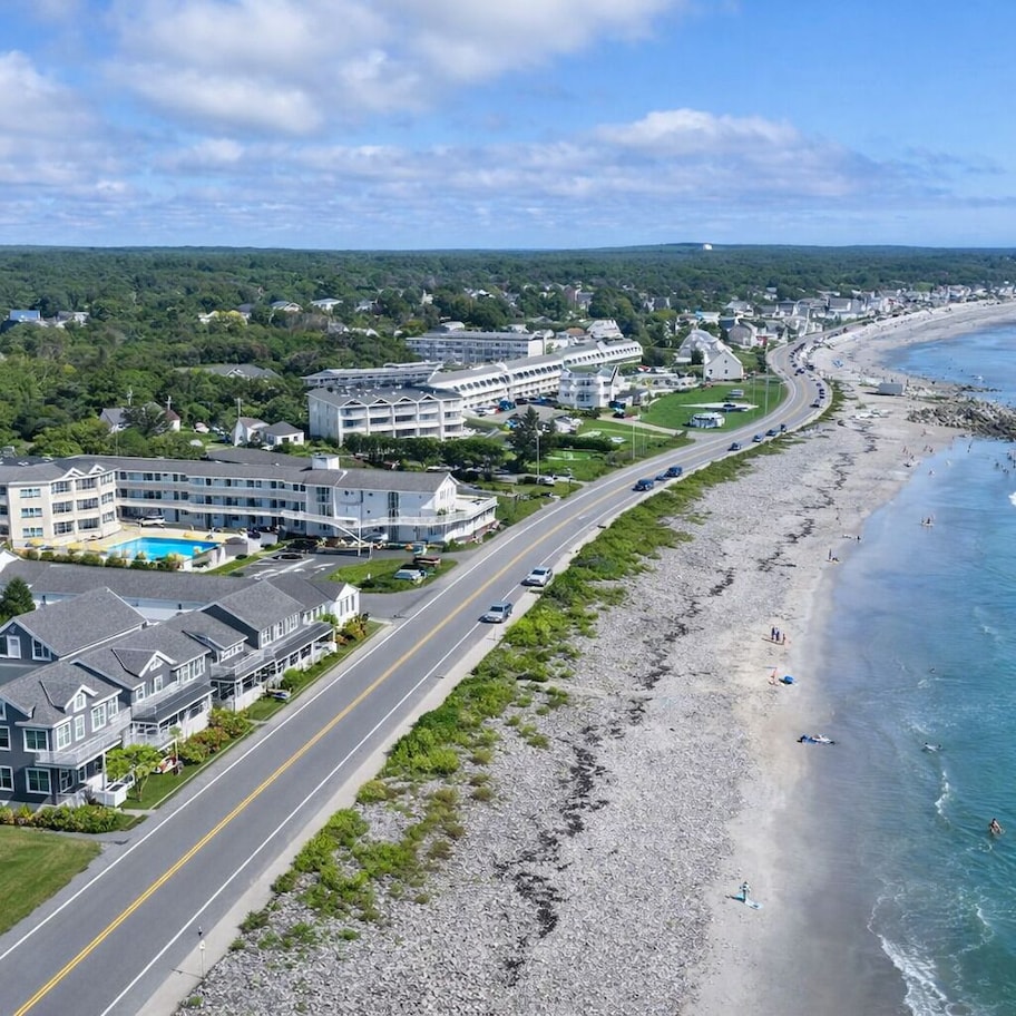 A coastal hotel with multiple buildings, a road adjacent to the beach, and ocean views.