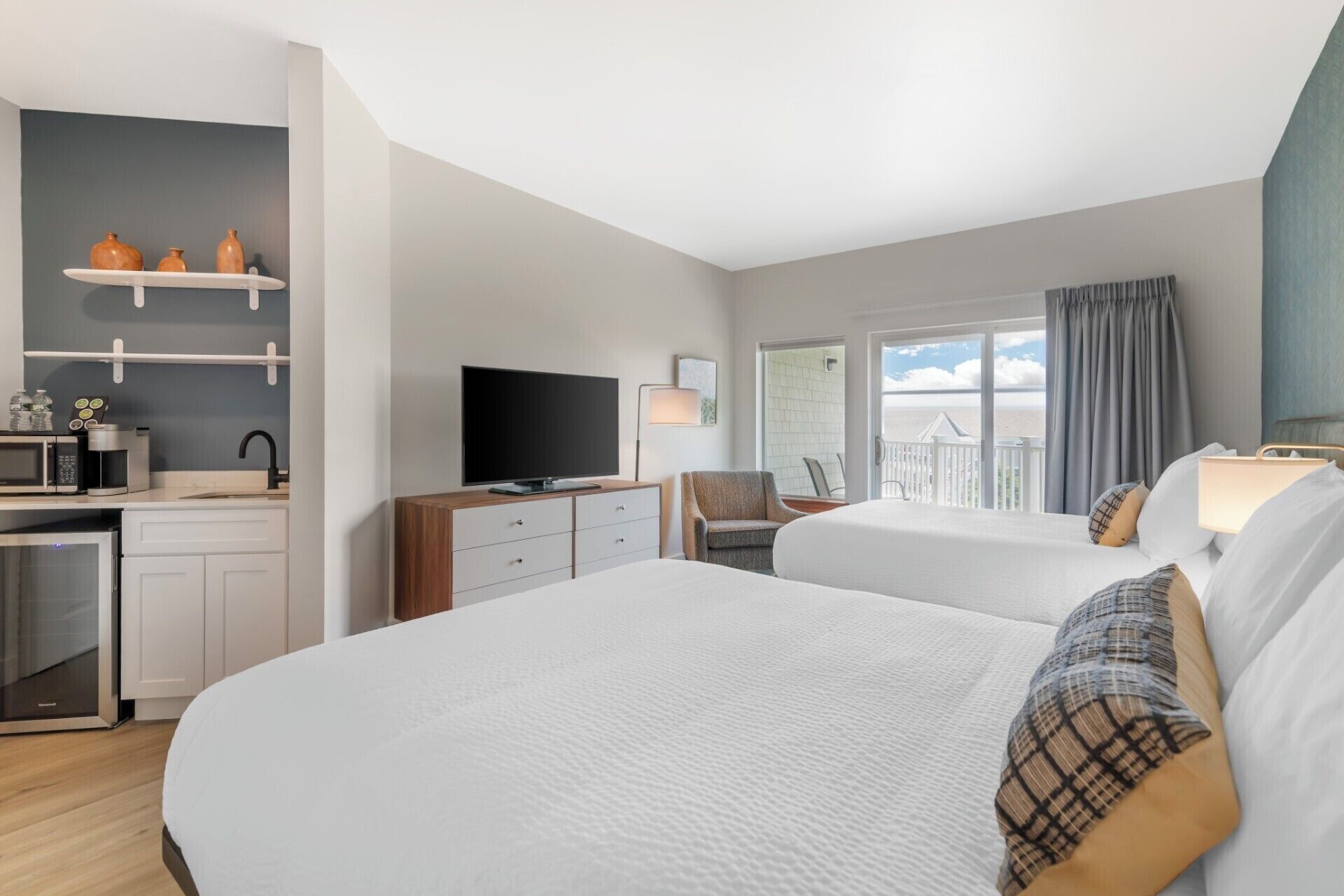 A hotel room with two beds, a TV, a desk with a microwave, a chair, and a balcony with a view.