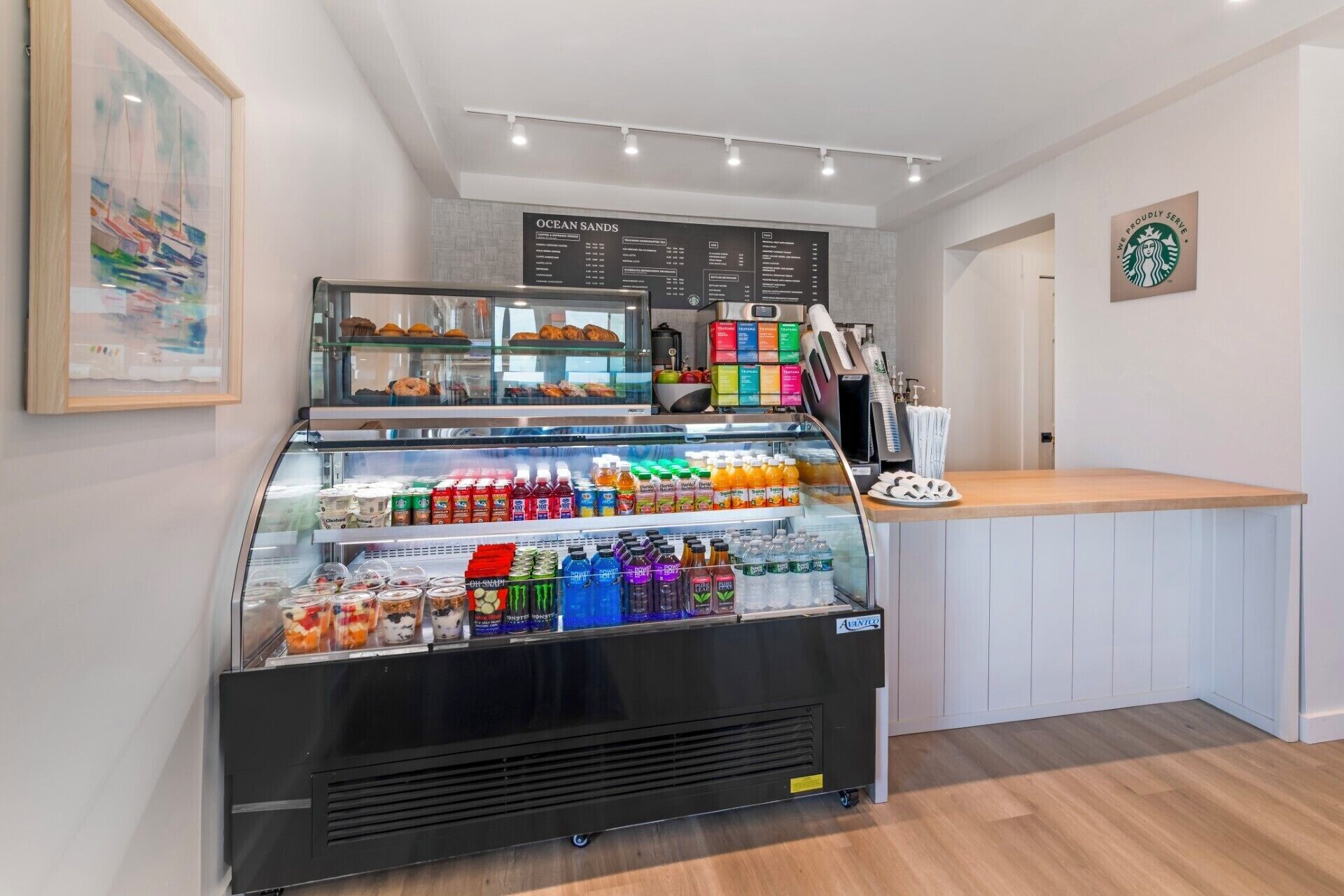 A café with a display case of beverages and pastries, a menu board, and a Starbucks logo on the wall.