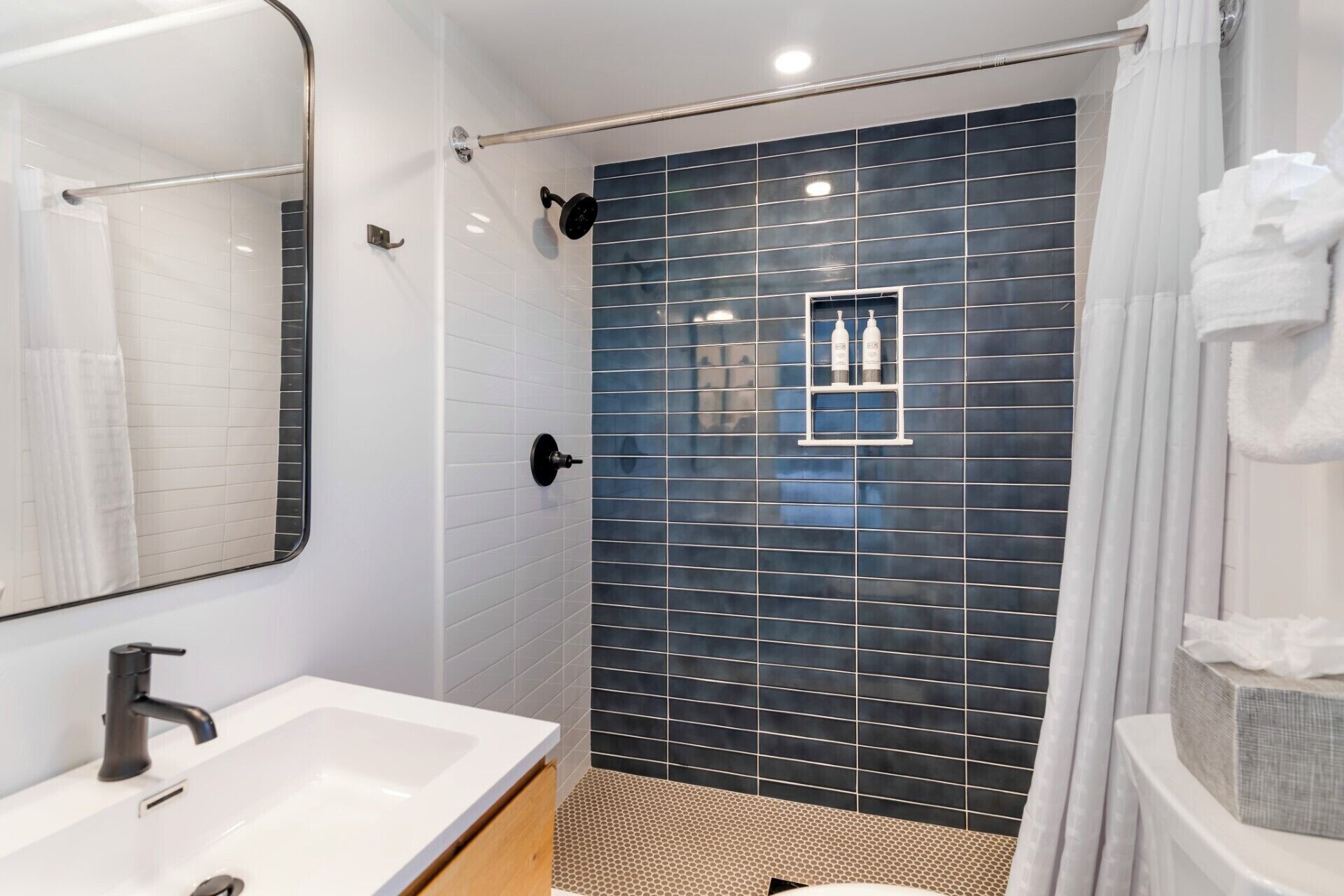 Un baño moderno con un lavabo blanco, una ducha negra y un espejo.