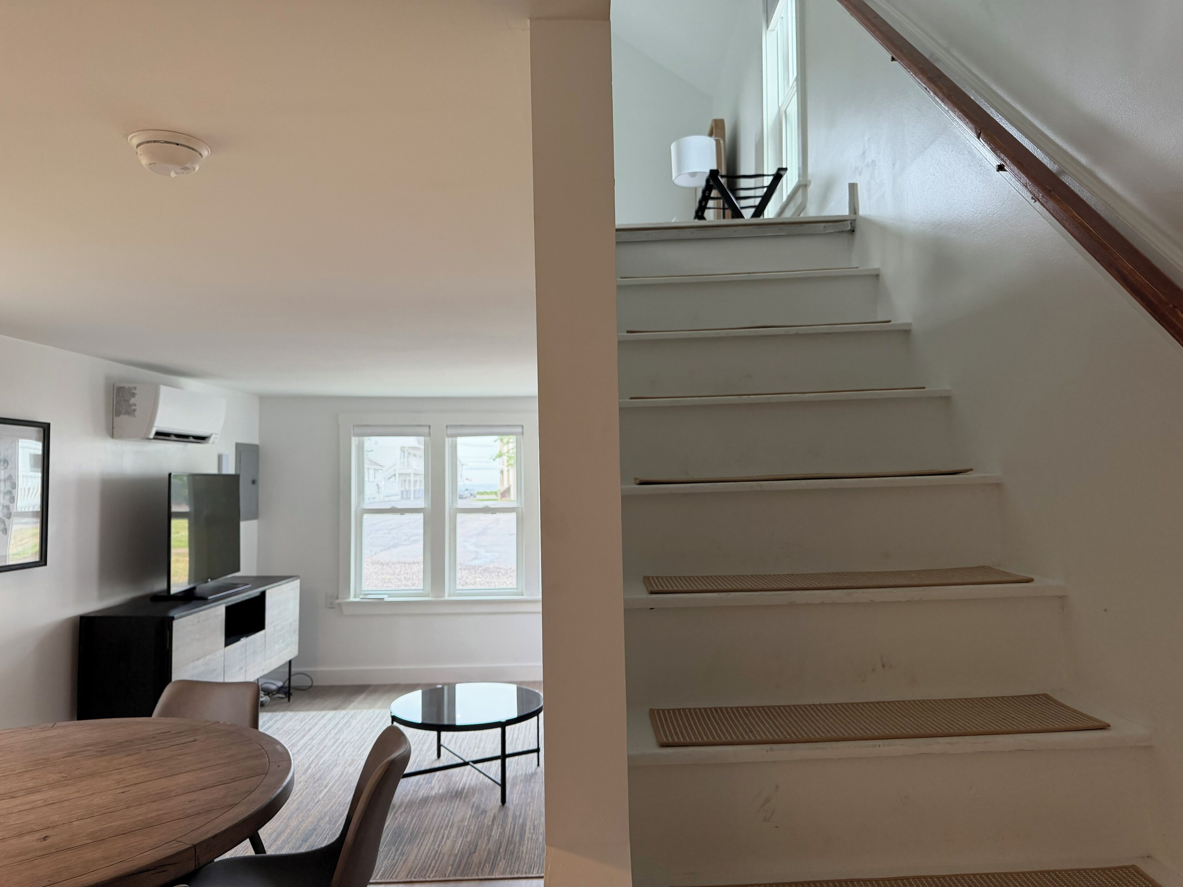 A modern living room with a dining area, a staircase, and a view of the outside.