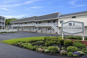 A motel with a sign reading 'Ocean Sands York Beach Collection,' featuring a two-story building with balconies and a parking lot.