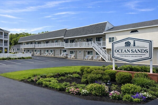 Un motel con un letrero que dice 'Ocean Sands York Beach Collection', que presenta un edificio de dos pisos con balcones y un estacionamiento.