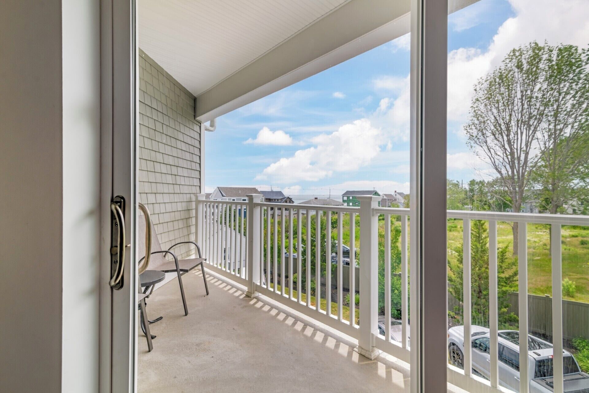A balcony with a white railing, a chair, and a view of a residential area with houses and cars.