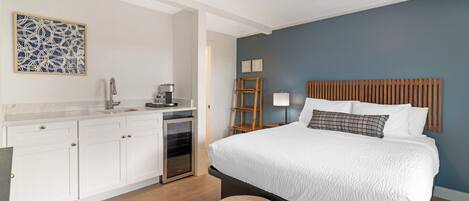 A bedroom with a bed, a wooden headboard, a coffee machine, a lamp, and a wall art piece.