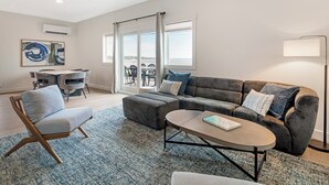 A modern living room with a sectional sofa, a round coffee table, and a dining area with chairs and a table. -  Ocean Sands at York Beach (York Beach)