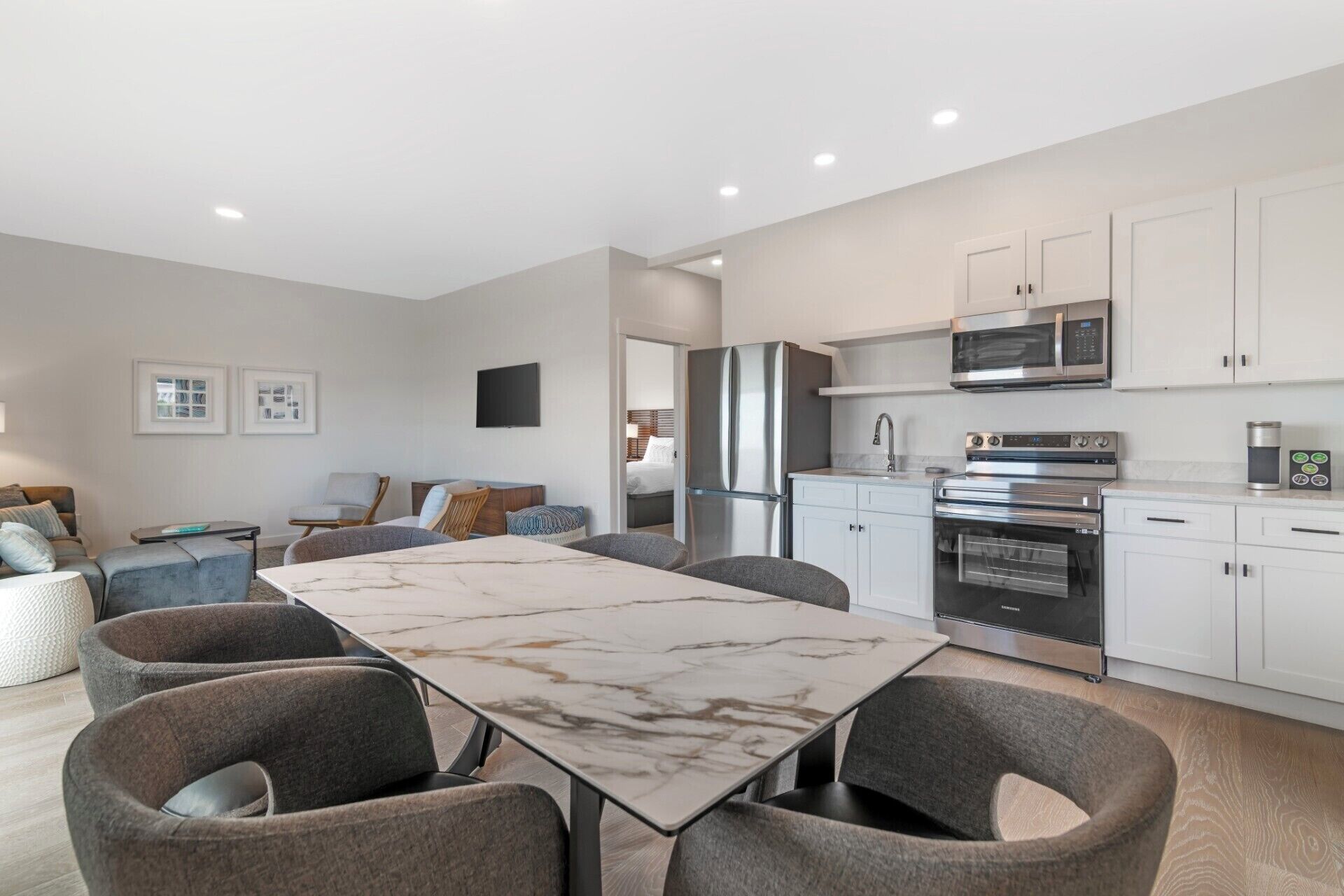 A modern kitchen with stainless steel appliances, a marble dining table, and grey upholstered chairs.