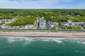 Vista aérea de una zona residencial costera con casas, una playa y un edificio grande con piscina.