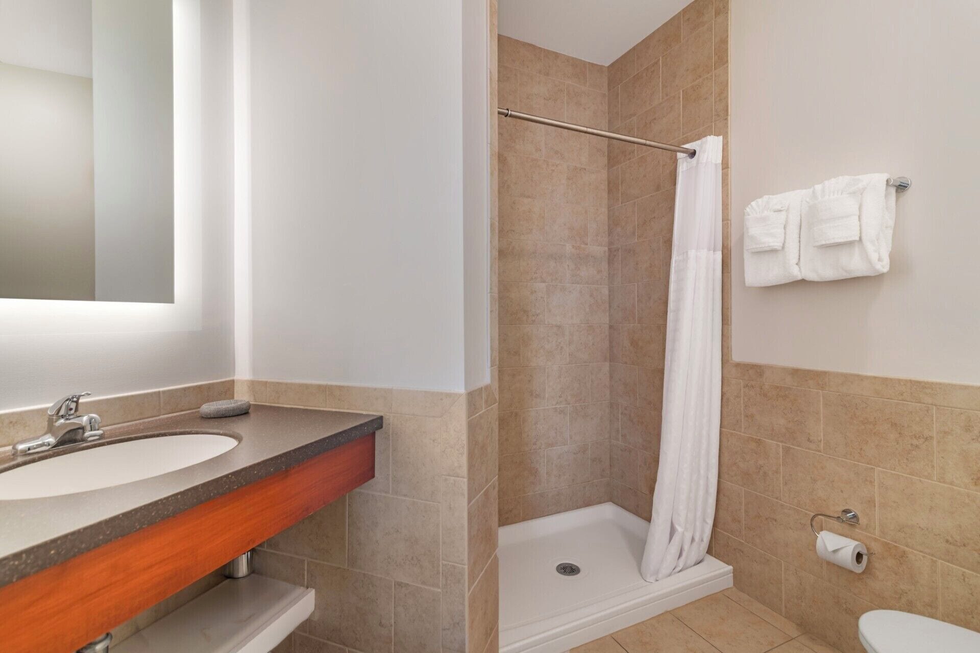 Une salle de bain équipée d’un lavabo, d’un miroir, d’une douche, de toilettes et d’un porte-serviettes.