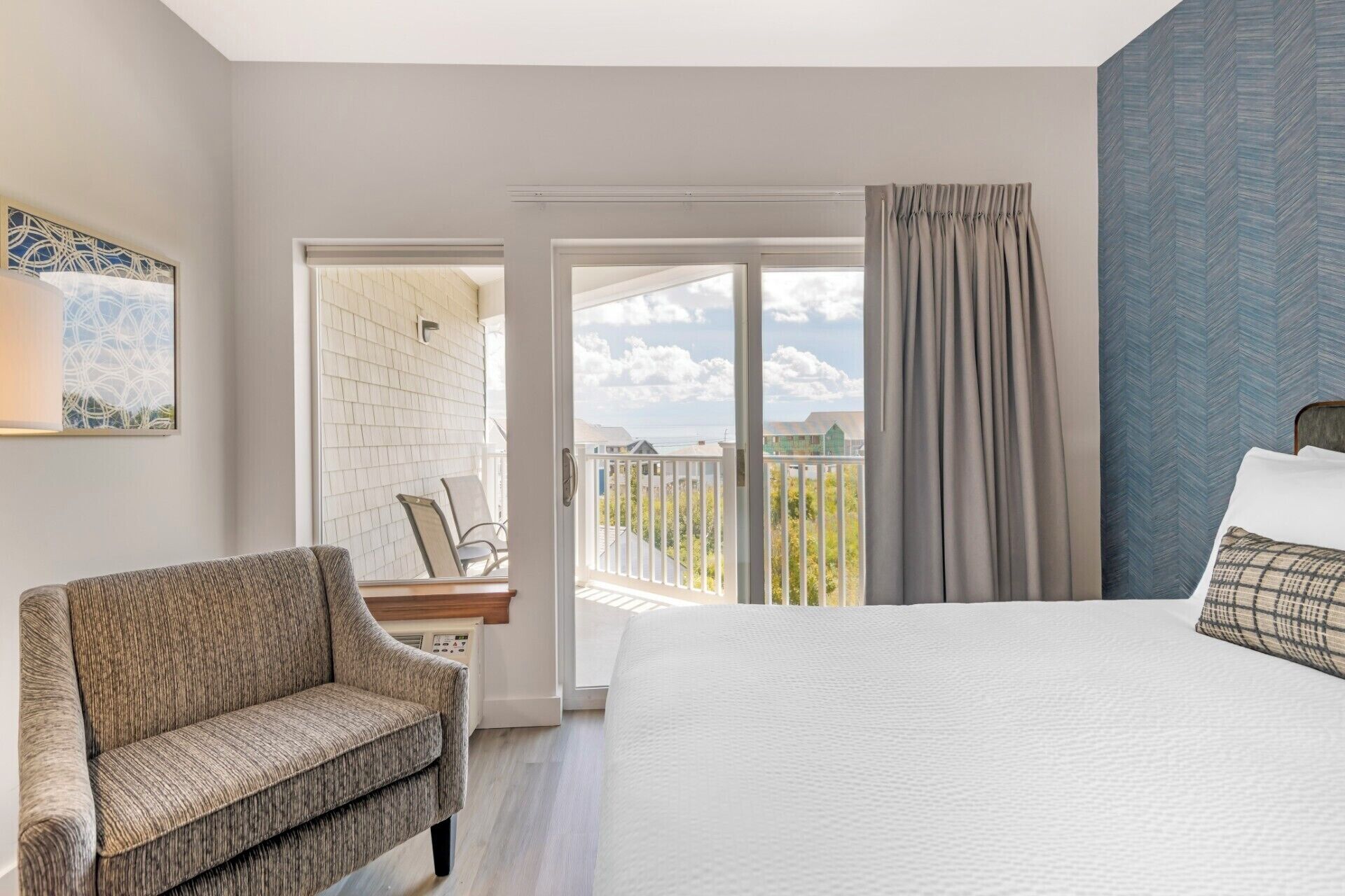 Un dormitorio con cama, una silla, un balcón con vistas y una puerta que da a un espacio exterior.