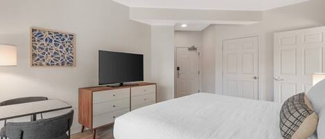 A hotel room with a bed, a desk with a chair, a television, a door, and a wall decoration.
