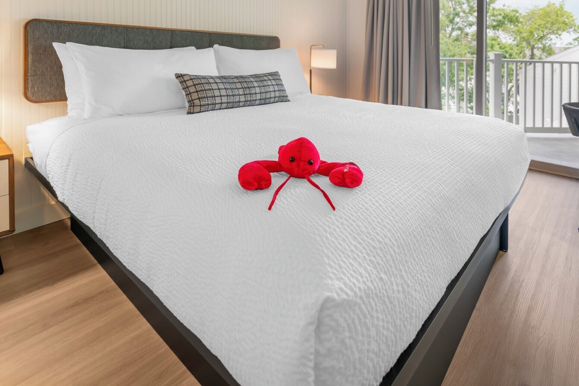 A neatly made bed with white bedding and a red plush toy in the center.