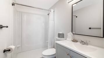 A bathroom with a shower, toilet, sink, and mirror.