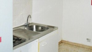 Una cocina pequeña con armarios blancos, un lavamanos de acero inoxidable y un refrigerador blanco.