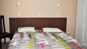 Una cama individual con cabecera marrón en una habitación con paredes lisas y dos interruptores de luz fijados a la pared.