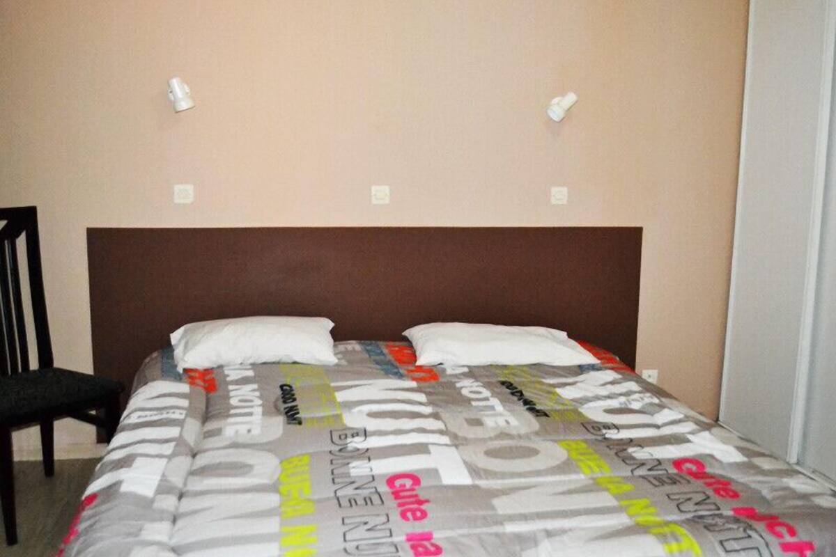 Una cama individual con cabecera marrón en una habitación con paredes lisas y dos interruptores de luz fijados a la pared.