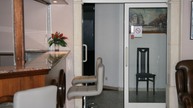 Un área de recepción con puerta de vidrio, un mostrador con un jarrón de flores y una silla.