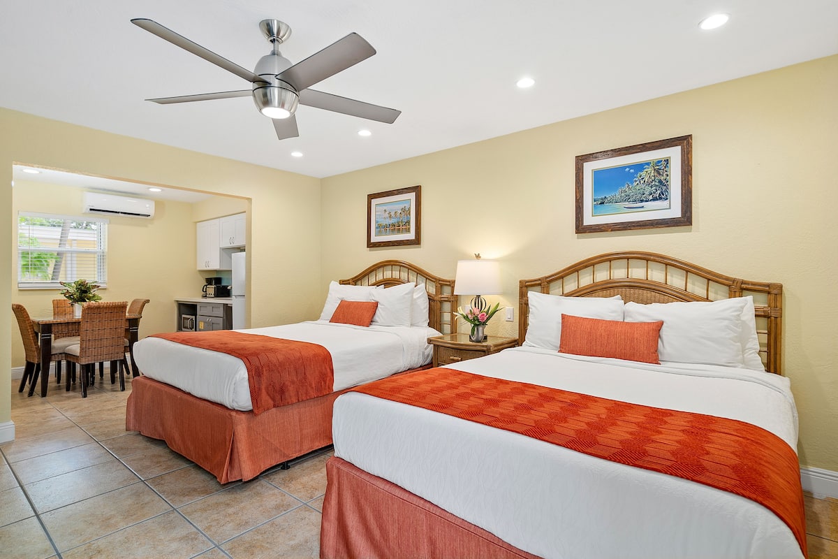 A hotel room with two beds, a ceiling fan, a dining area, and a kitchen.