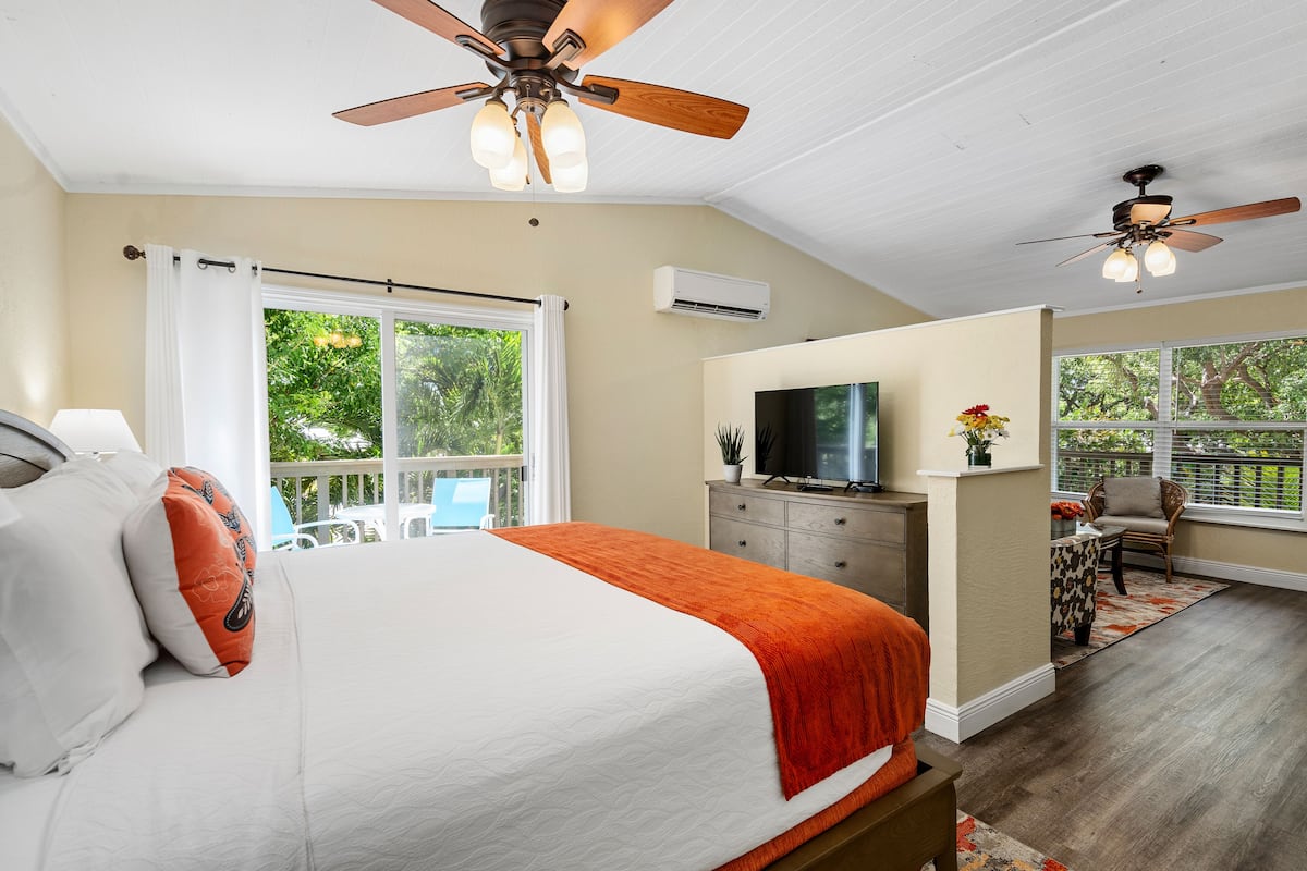 A bedroom with a bed, ceiling fans, a TV, and a view of the outdoors.