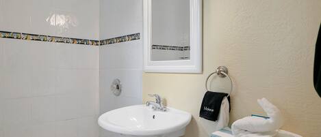 Un baño con un lavamanos blanco, una bañera y una ducha. Hay un perchero con toallas y una toalla negra con la palabra "Makeup" escrita.