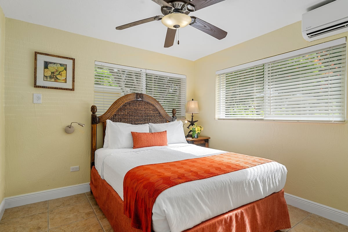 A bedroom with a bed, a ceiling fan, and two windows with blinds.