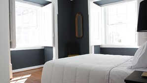 A bedroom with a large bed, two windows, a mirror, and a nightstand. - Largo da Sé - HOrigem (Lisbon)