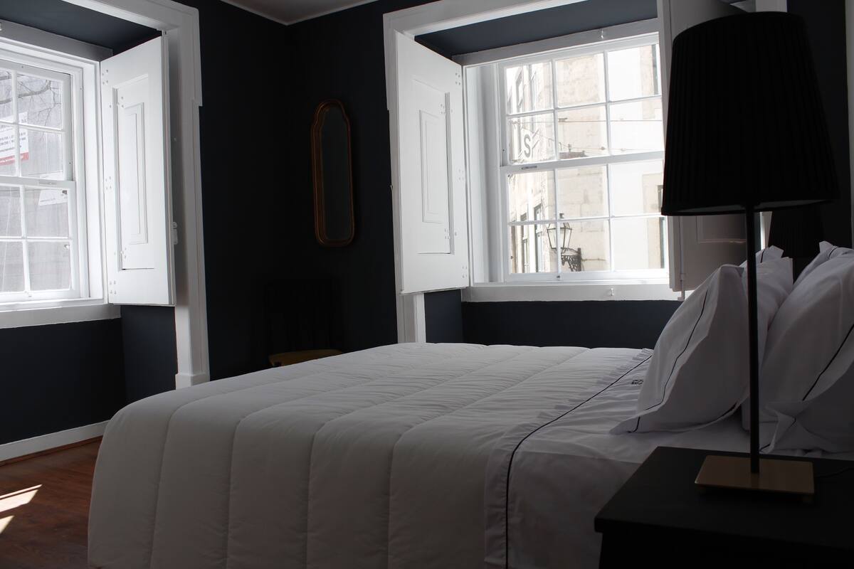 A bedroom with a bed, a nightstand, a lamp, and two windows.