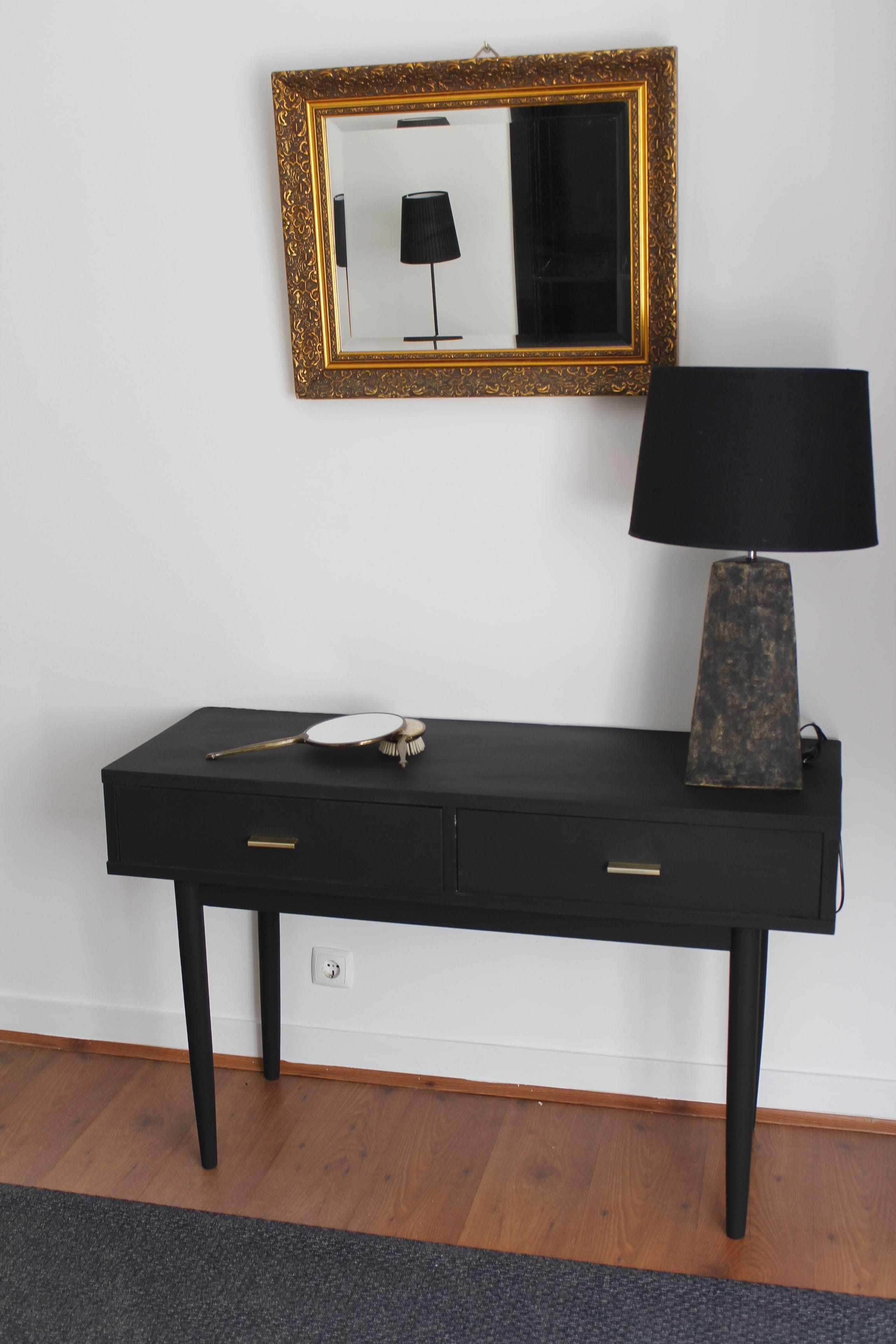 Un bureau noir avec deux tiroirs, un miroir rond et une lampe.