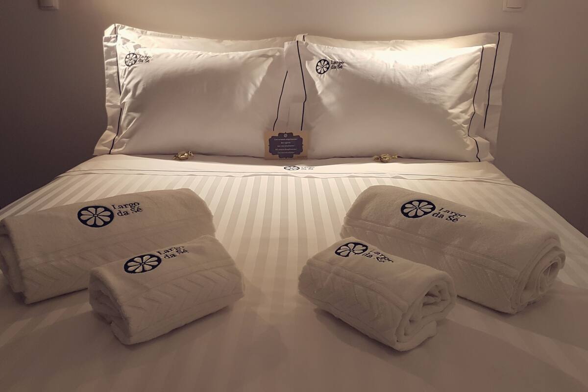 A neatly made bed with white linens, two towels with a logo, and a small decorative item on the headboard.