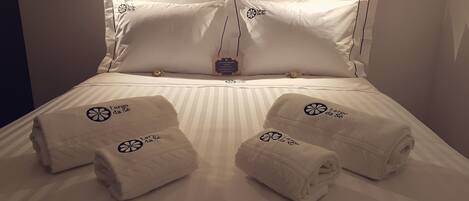 A neatly made bed with white linens, two towels with a logo, and a small decorative item on the headboard.