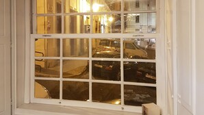 A window with multiple panes, reflecting a street scene with parked cars and buildings. - Largo da Sé - HOrigem (Lisbon)