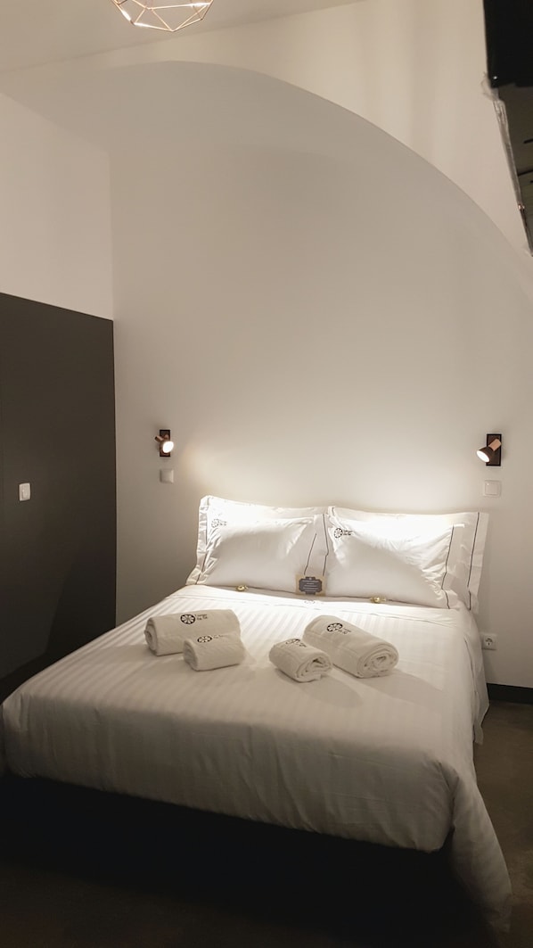A modern hotel room with a large bed, two bedside lamps, and a unique curved ceiling design. - Largo da Sé - HOrigem (Lisbon)