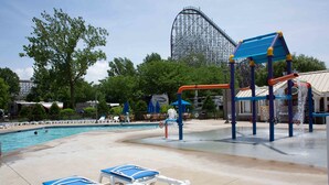 A pool area with lounge chairs, a water play structure, and a roller coaster in the background. - Cedar Point's Lighthouse Point (Sandusky)