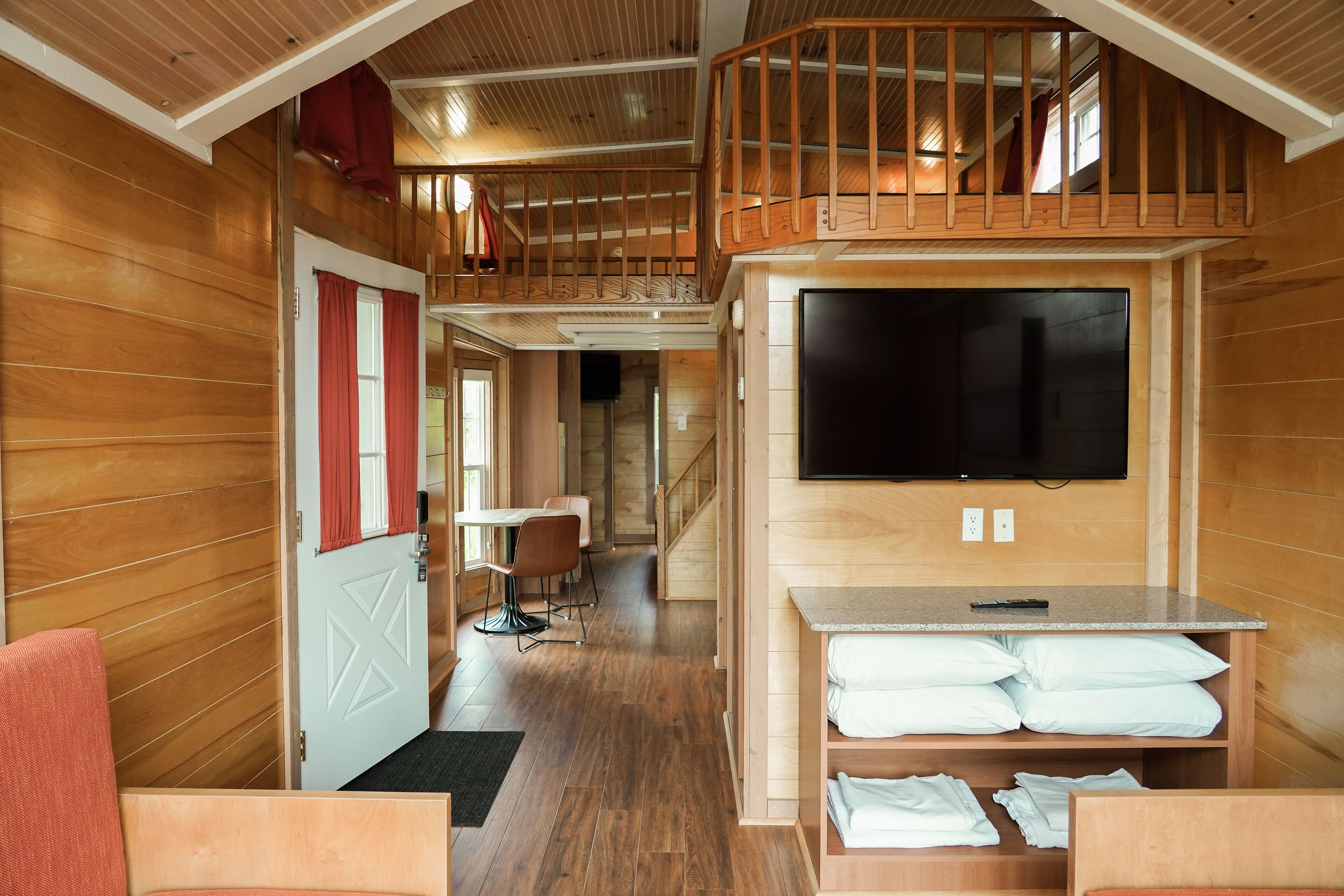 Een houten interieur met een eethoek, een aan de muur bevestigde televisie en een trap naar een hoger niveau.