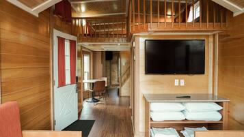 A wooden interior with a dining area, a TV mounted on the wall, and a staircase leading to an upper level.