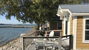 A wooden deck with outdoor seating, a building with a metal roof, and a view of a dock and water. - Cedar Point's Lighthouse Point (Sandusky)