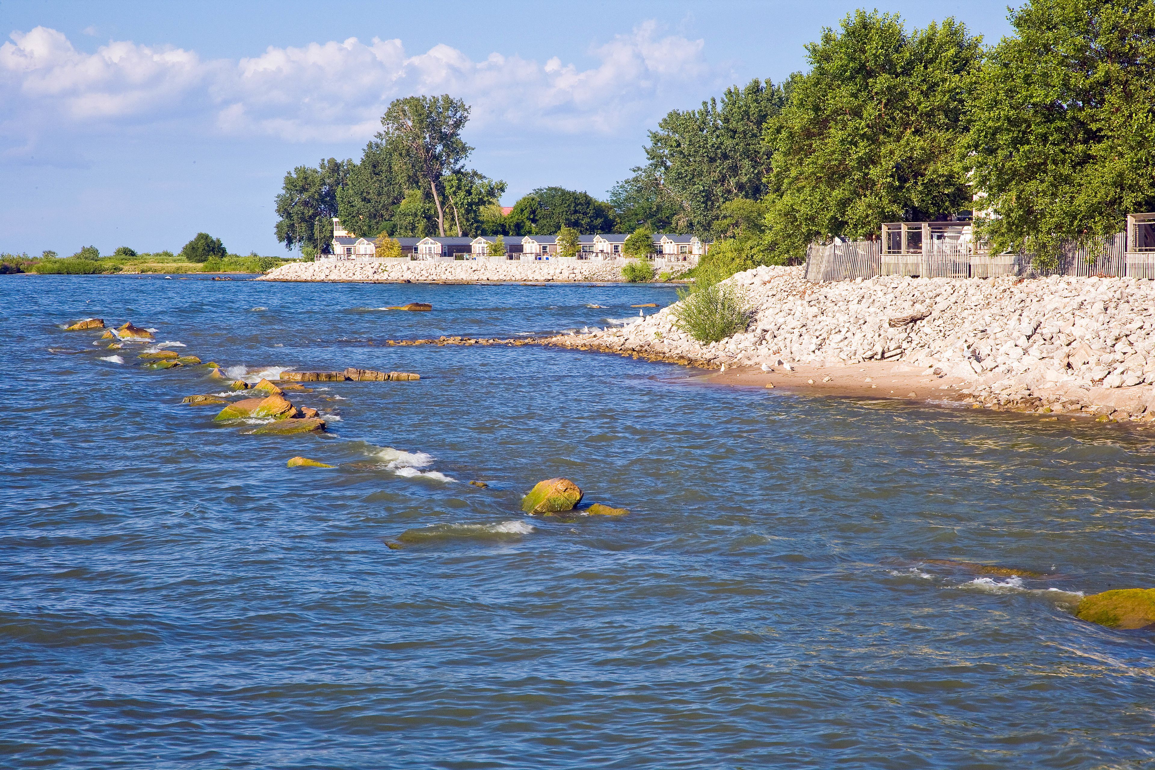 Un hôtel situé au bord de la rivière, avec une rive rocheuse, des arbres et un ciel dégagé.