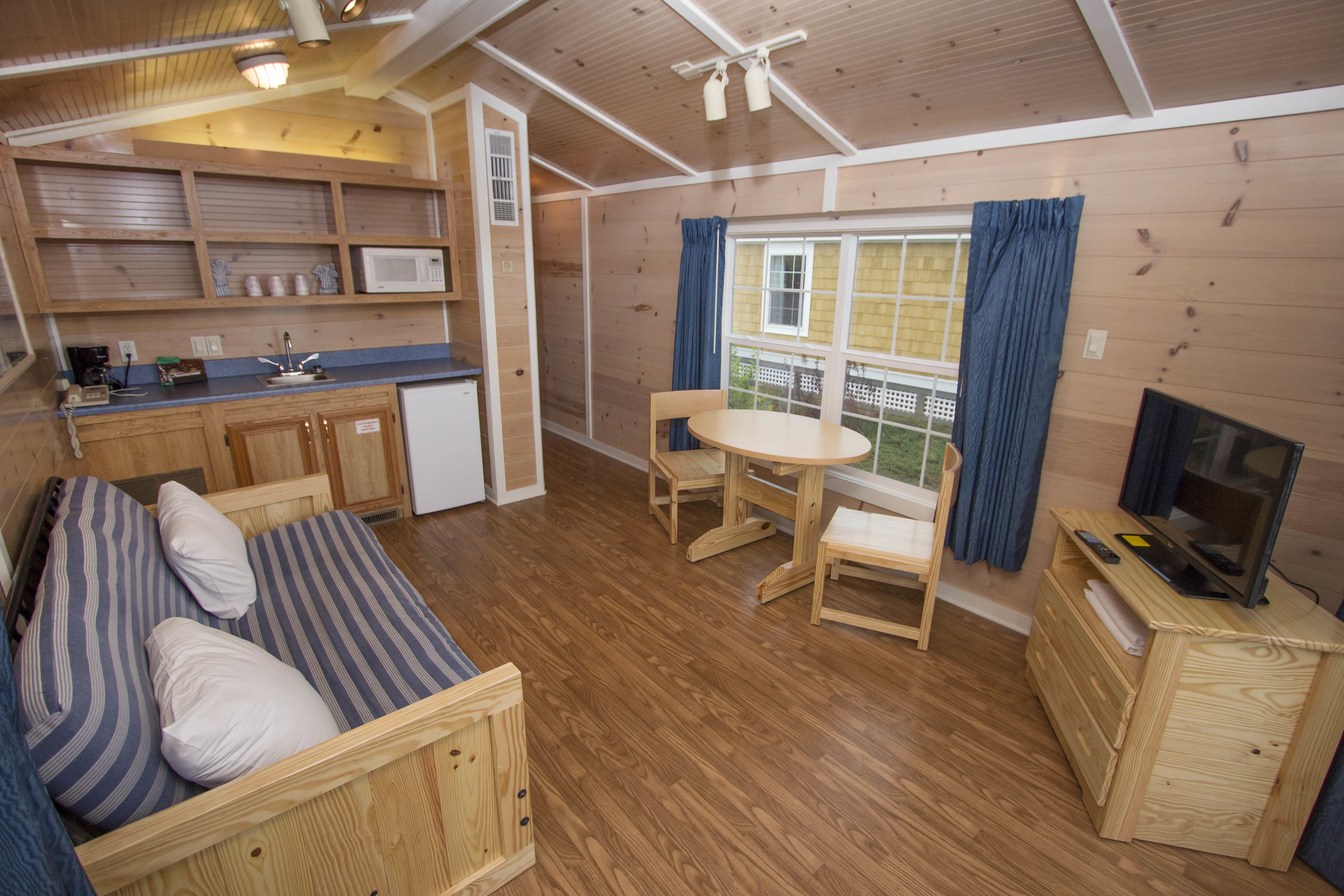 Una cabaña acogedora con interior de madera, kitchenette, comedor y televisor.