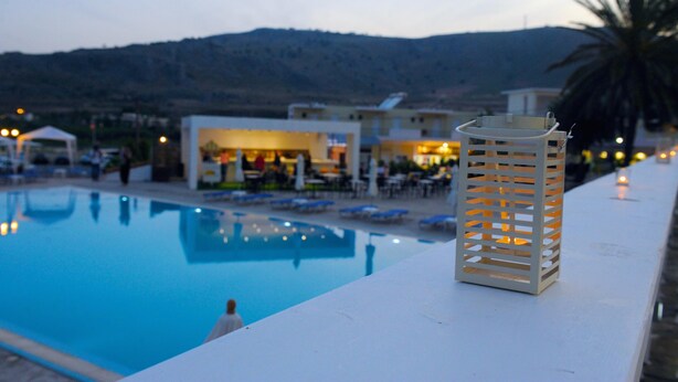 A swimming pool with lounge chairs, a white lantern, and a building with outdoor seating in the background. - Ellia Hotel (Rhodes)