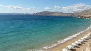 A beach with clear water, a row of umbrellas, and a mountainous backdrop. - Ellia Hotel (Rhodes)