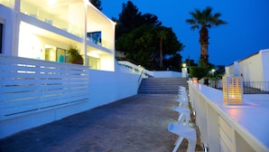 A building with a staircase leading to a balcony, white outdoor seating, and a palm tree. - Ellia Hotel (Rhodes)