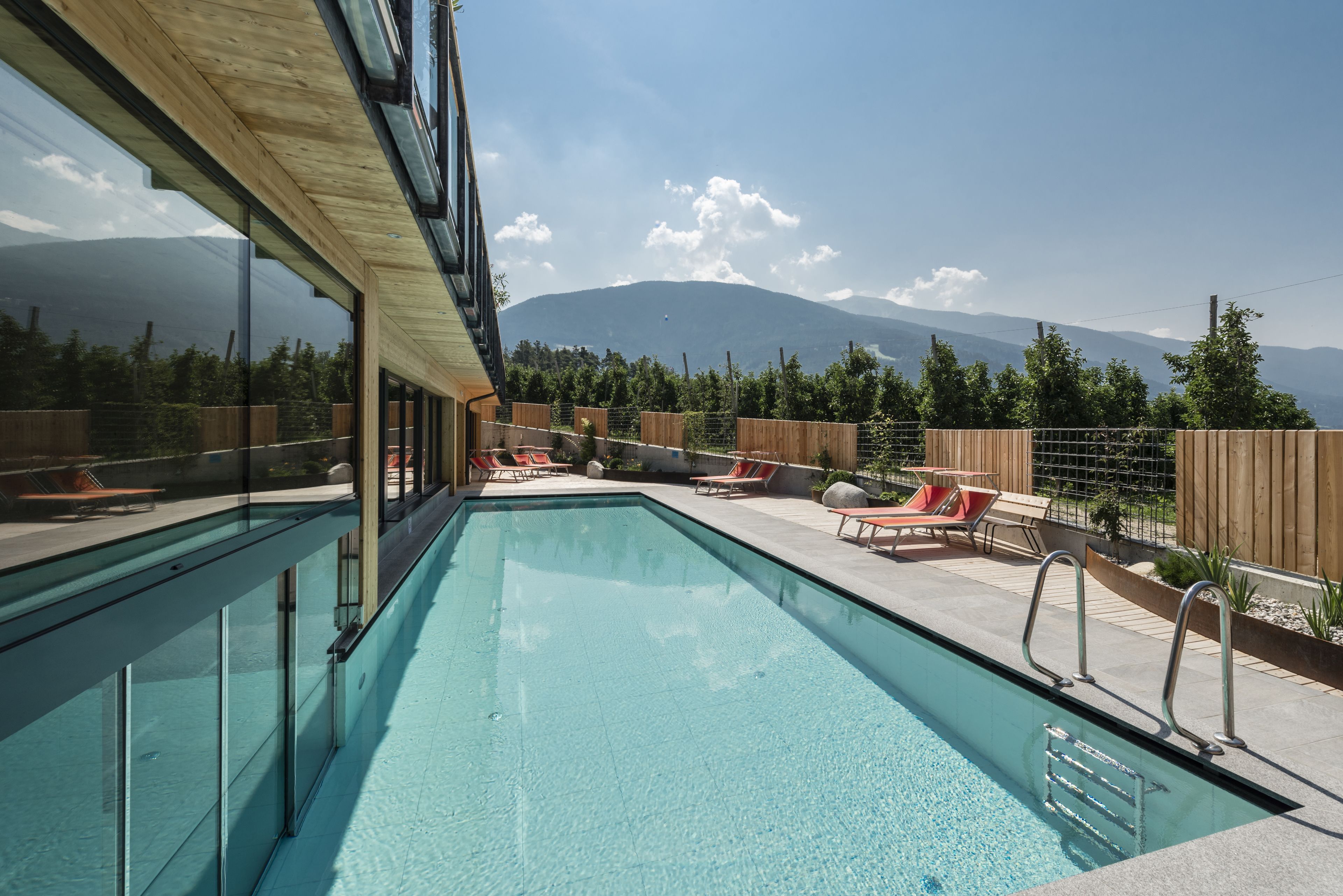 Área de piscina com vista clara para montanhas ao fundo, deck de madeira e espreguiçadeiras.