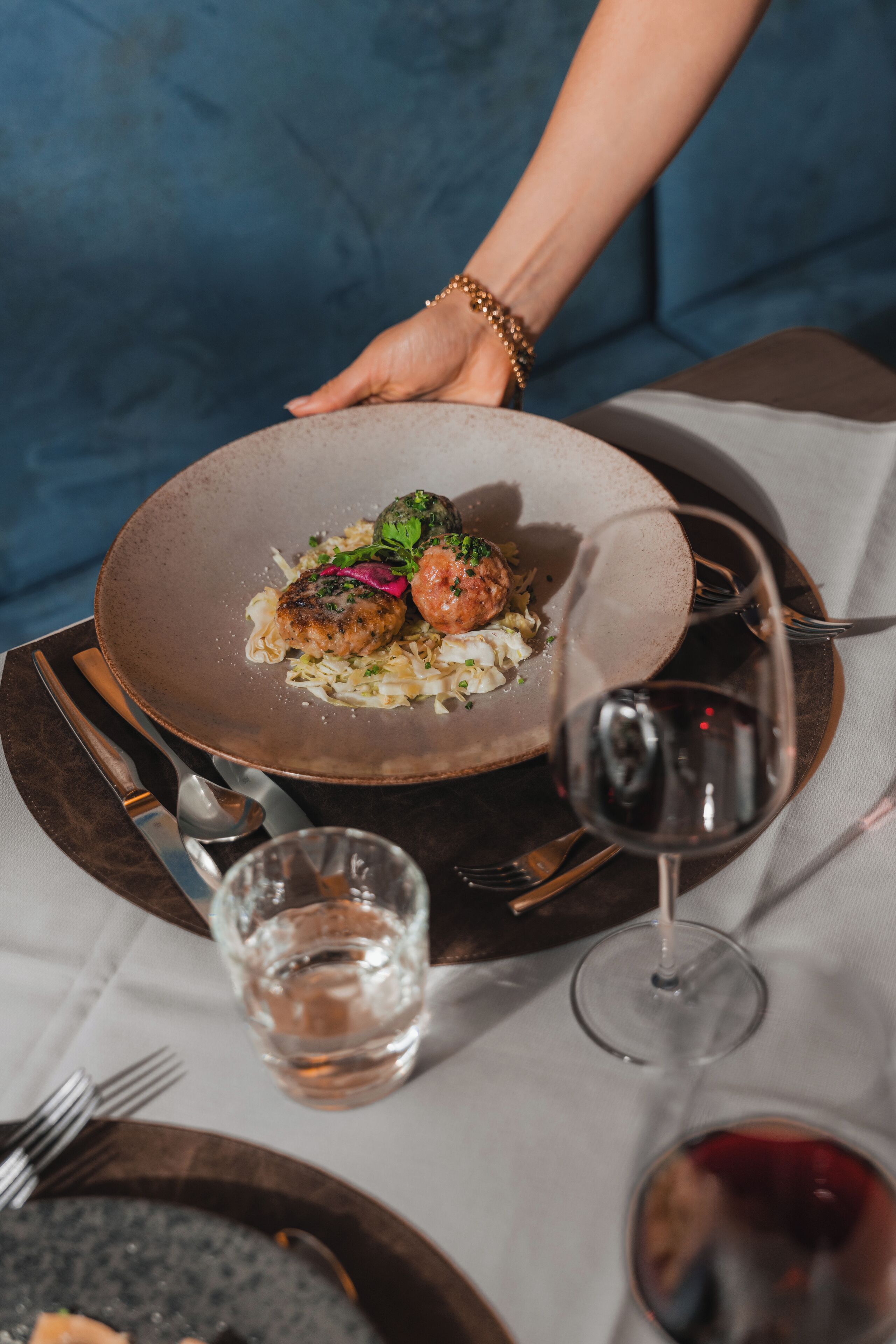 A dining table with a plate of food, a glass of red wine, and cutlery.