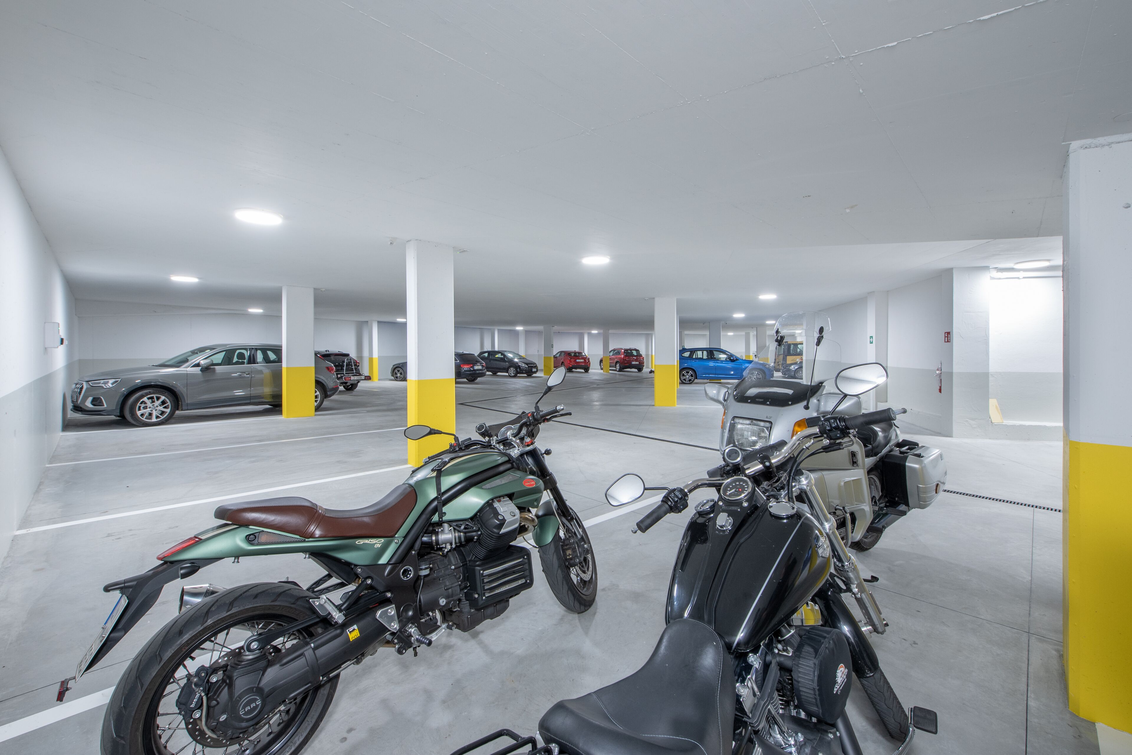 Un parking à plusieurs niveaux où sont garées plusieurs voitures et motos.