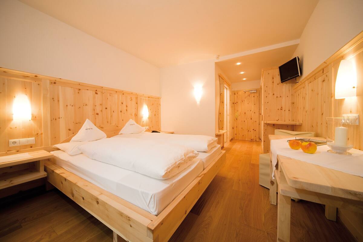 Une pièce en bois avec un lit, des tables de chevet, une table avec des fruits et un téléviseur fixé au mur.